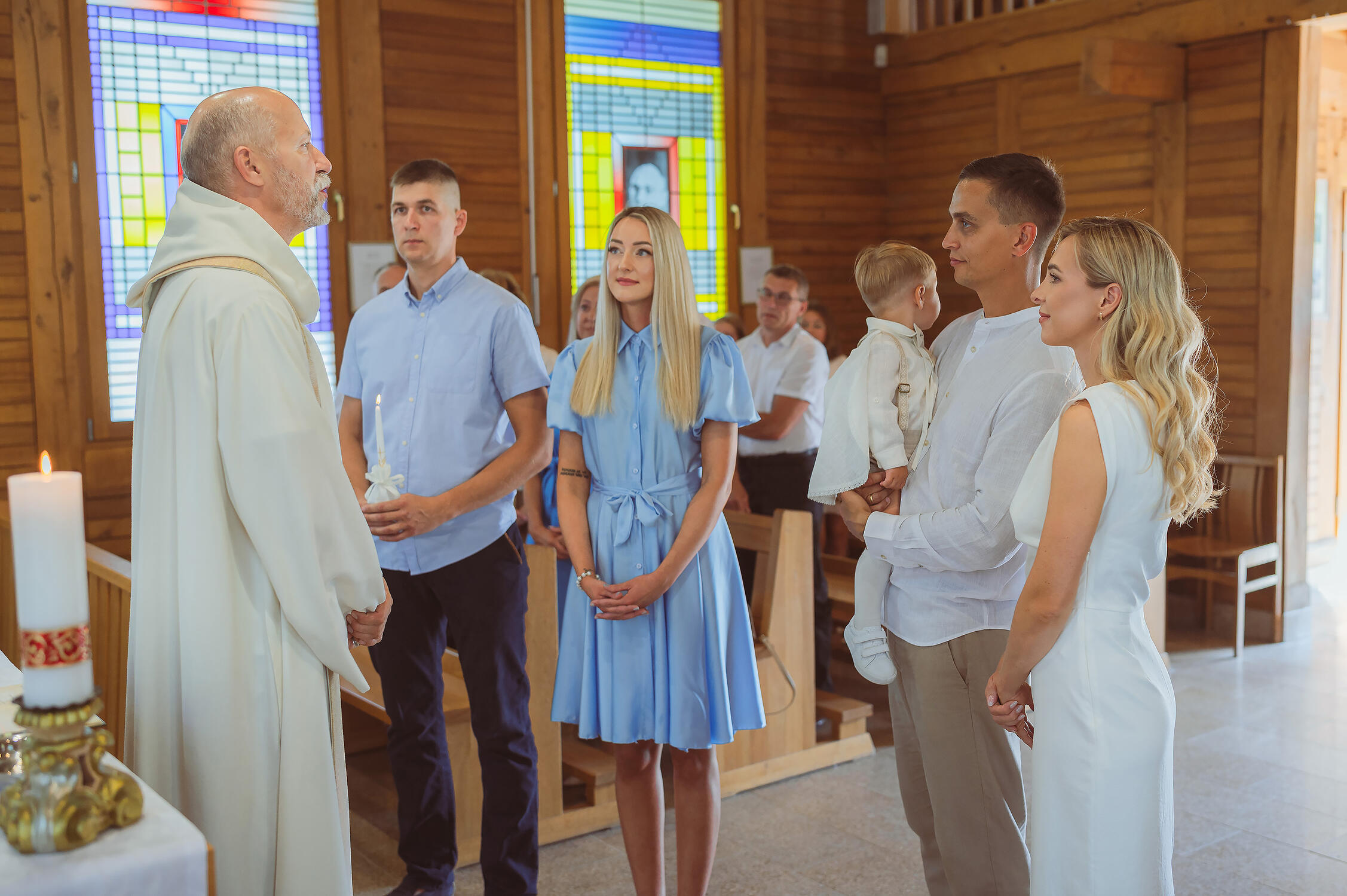 Kūdikio krikšto ceremonija bažnyčioje Profesionalios krikštynų fotografijos – šeimos portretas su pakrikštytu kūdikiu.
