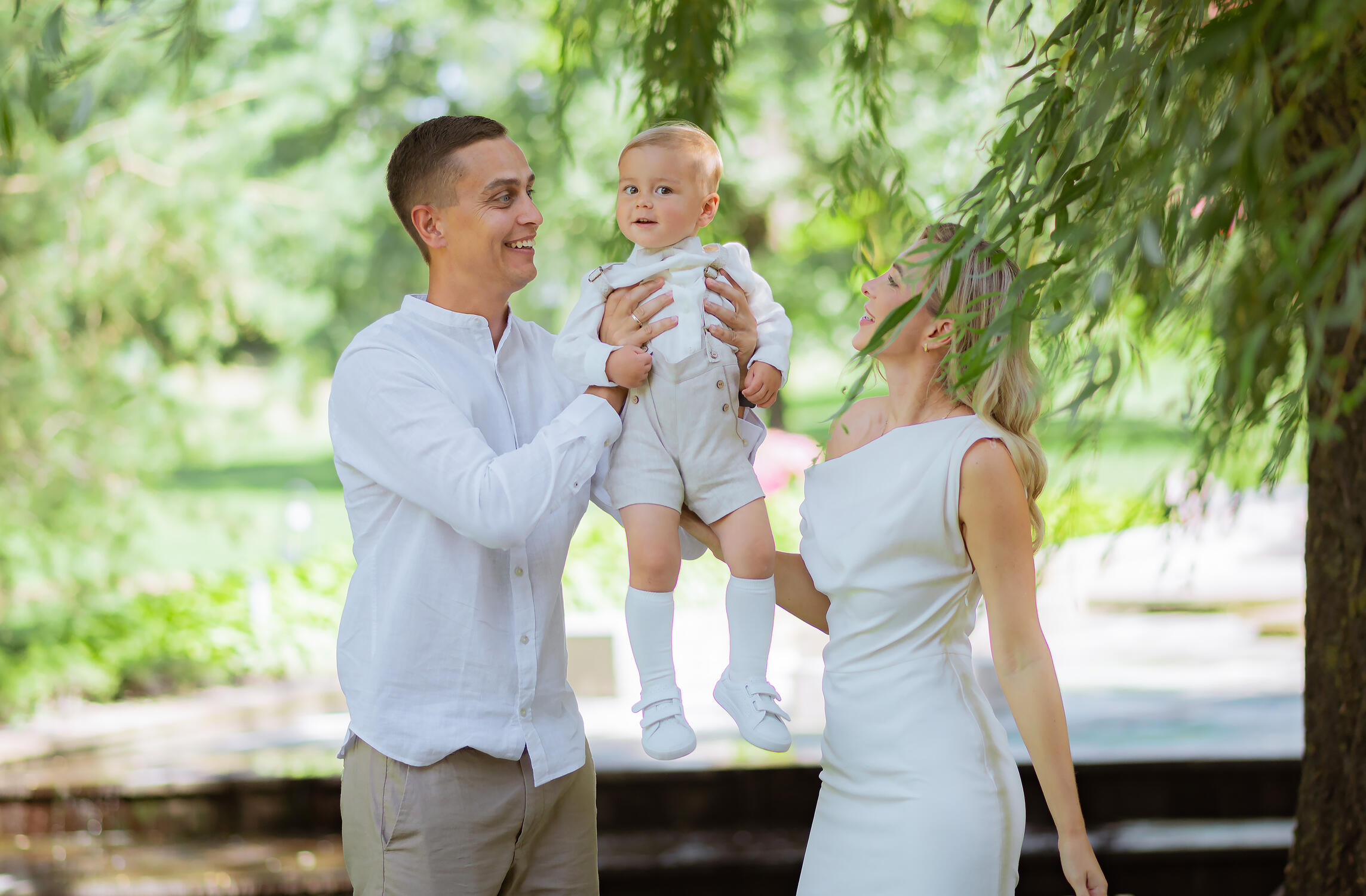 Šeimos fotosesija Šeimos fotografė įamžina tėvus, žaidžiančius su vaiku parke. Natūrali šeimos fotosesija lauke, skirta išsaugoti vaikystės prisiminimus, šeimos bendrystę ir spontaniškas emocijas