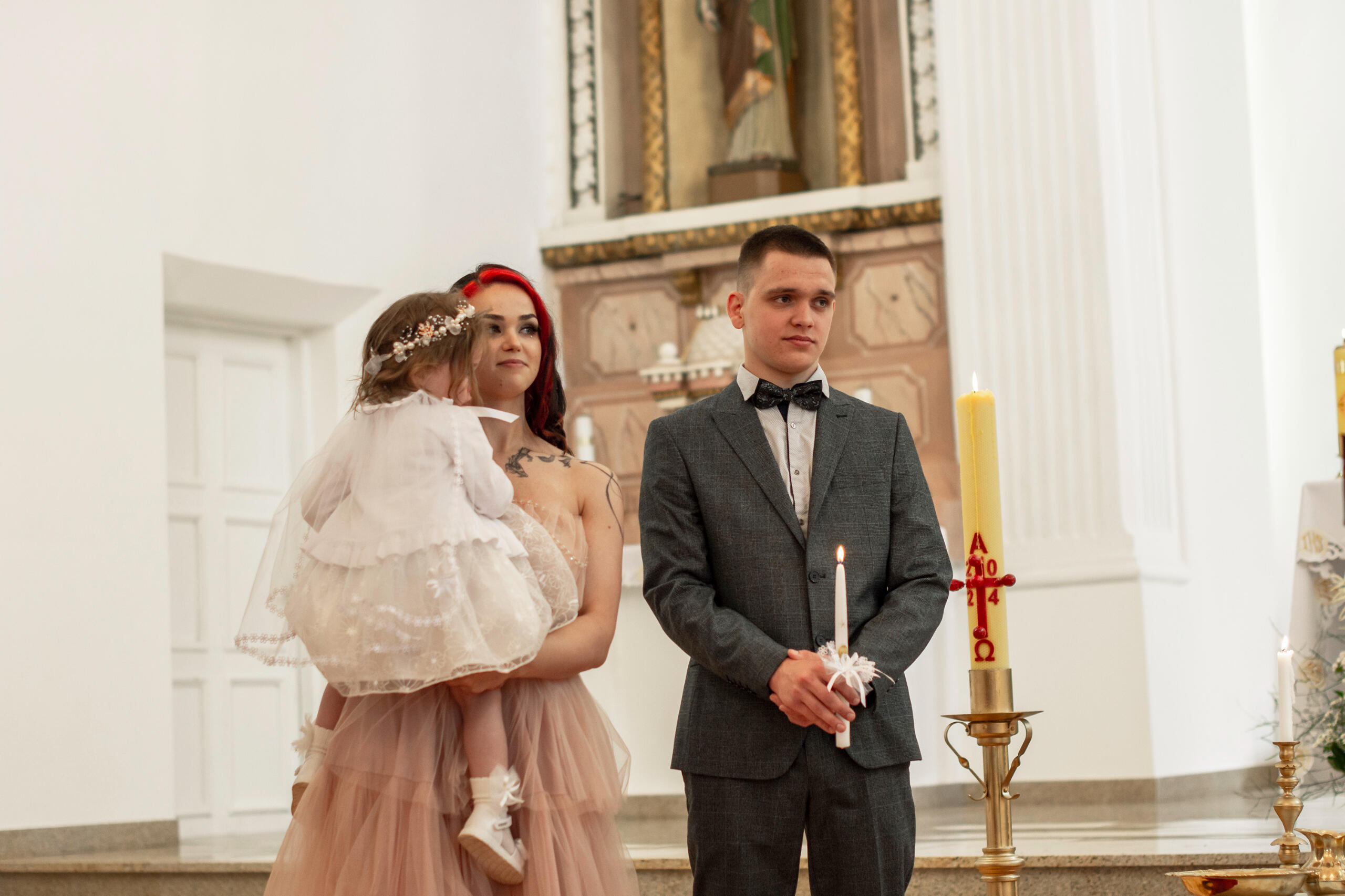 Krikšto tėvai pozuoja su krikšto dukra bažnyčioje